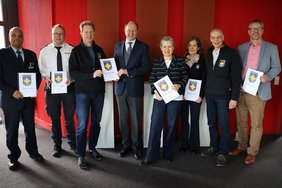 Johannes Schütze (Kreispolizeibehörde Warendorf Direktion Gefahrenabwehr/Einsatz, v. l.), Nils Recker (stv. Leiter der Kreisleitstelle), Martin Remke (Koordinator für die Notfallseelsorge im Kreis Warendorf), Landrat Dr. Olaf Gericke, Ordnungsdezernentin Petra Schreier, Petra Huß (Notfallseelsorgerin), Martin Kofoth (Feuerwehrseelsorger) und Michael Frerich (Amtsleiter Bevölkerungsschutz) bei der Übergabe des Jahresberichts. 		Foto: Kreis Warendorf