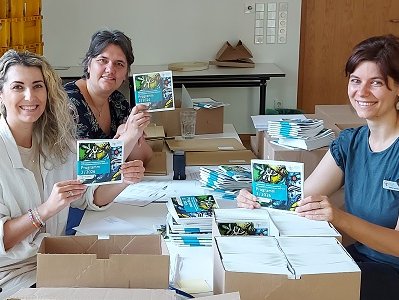 Katharina Rommel, Maxie Kordes und Sylvia Henselmeier von der Ev. Erwachsenenbildung im Kirchenkreis Gütersloh bereiten den Versand der Programmehefte für das zweite Halbjahr 2026 vor. 		Foto: Kirchenkreis Gütersloh/Frauke Brauns